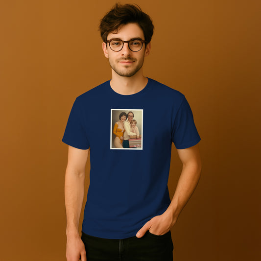 A man wearing a blue t-shirt with a framed photograph of a family on it, standing against a brown background.