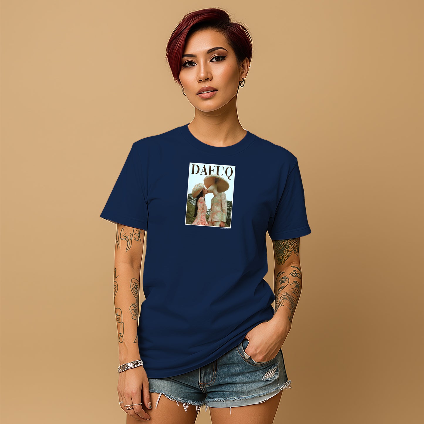 A young woman with short red hair wearing a navy blue t-shirt with a graphic design and denim shorts stands against a beige background.