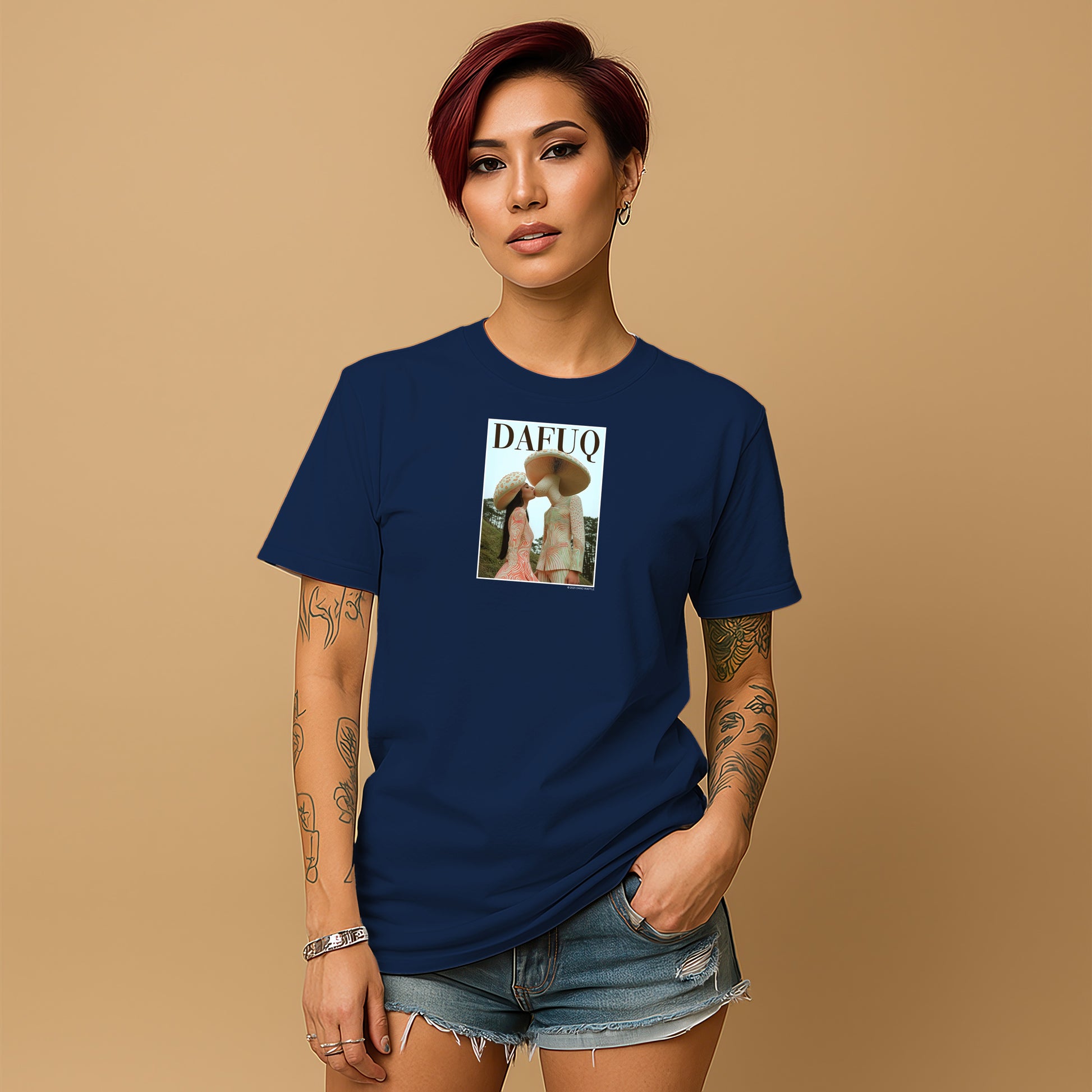 A young woman with short red hair wearing a navy blue t-shirt with a graphic design and denim shorts stands against a beige background.