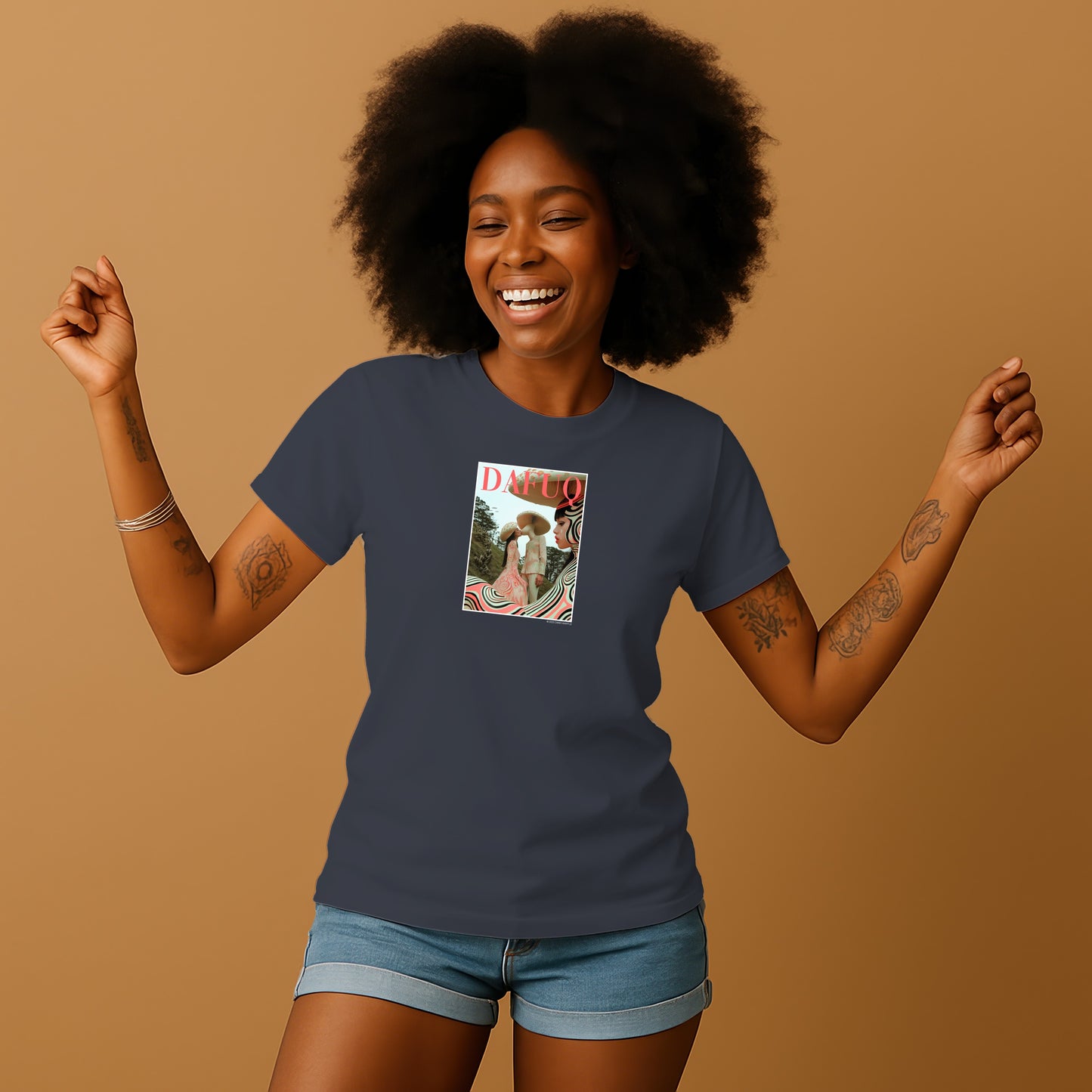 A smiling woman with curly hair wearing a blue t-shirt with a graphic design on it, standing against a beige background.