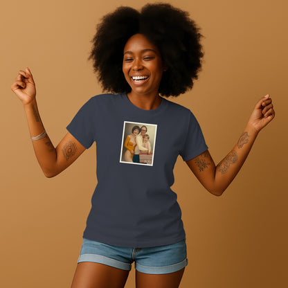 A smiling woman with curly hair wearing a blue t-shirt with a framed photo of two people on it, standing against a beige background.
