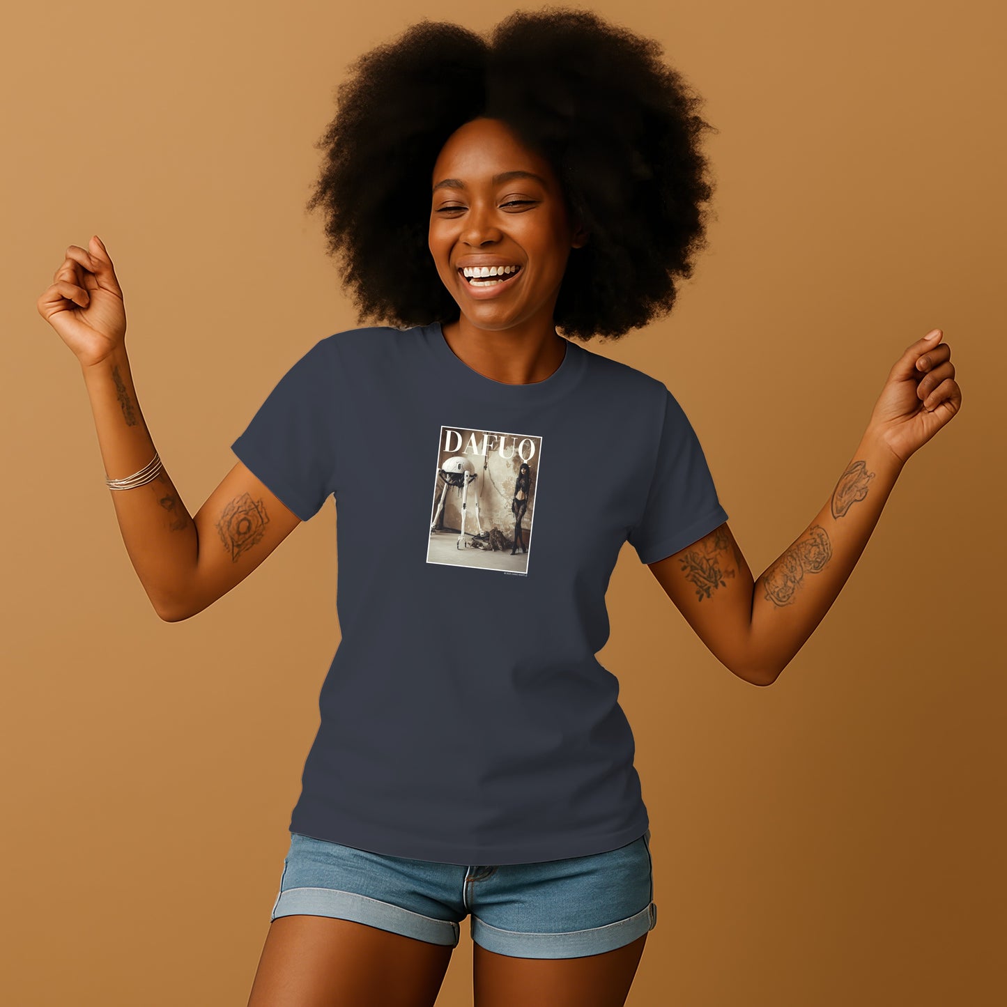 A smiling woman with curly hair wearing a blue t-shirt with a graphic design on it, standing with her arms raised in a joyful pose.