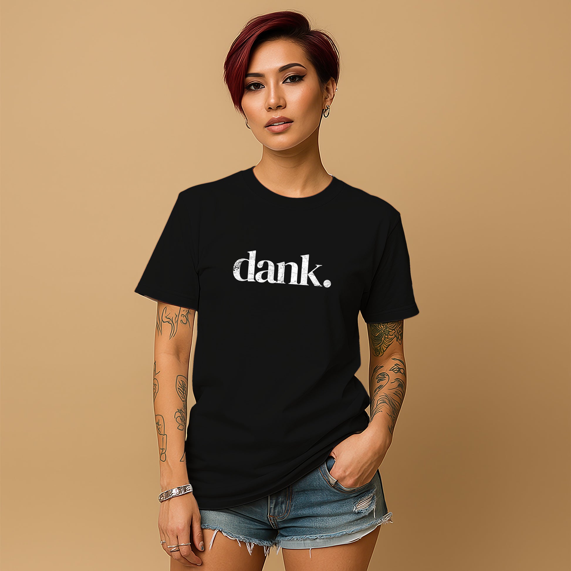 A young woman with short red hair wearing a black t-shirt with the word "dank" printed on it, standing against a beige background.