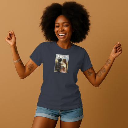 A smiling woman with curly hair wearing a dark blue t-shirt with a graphic design on it, standing against a beige background.