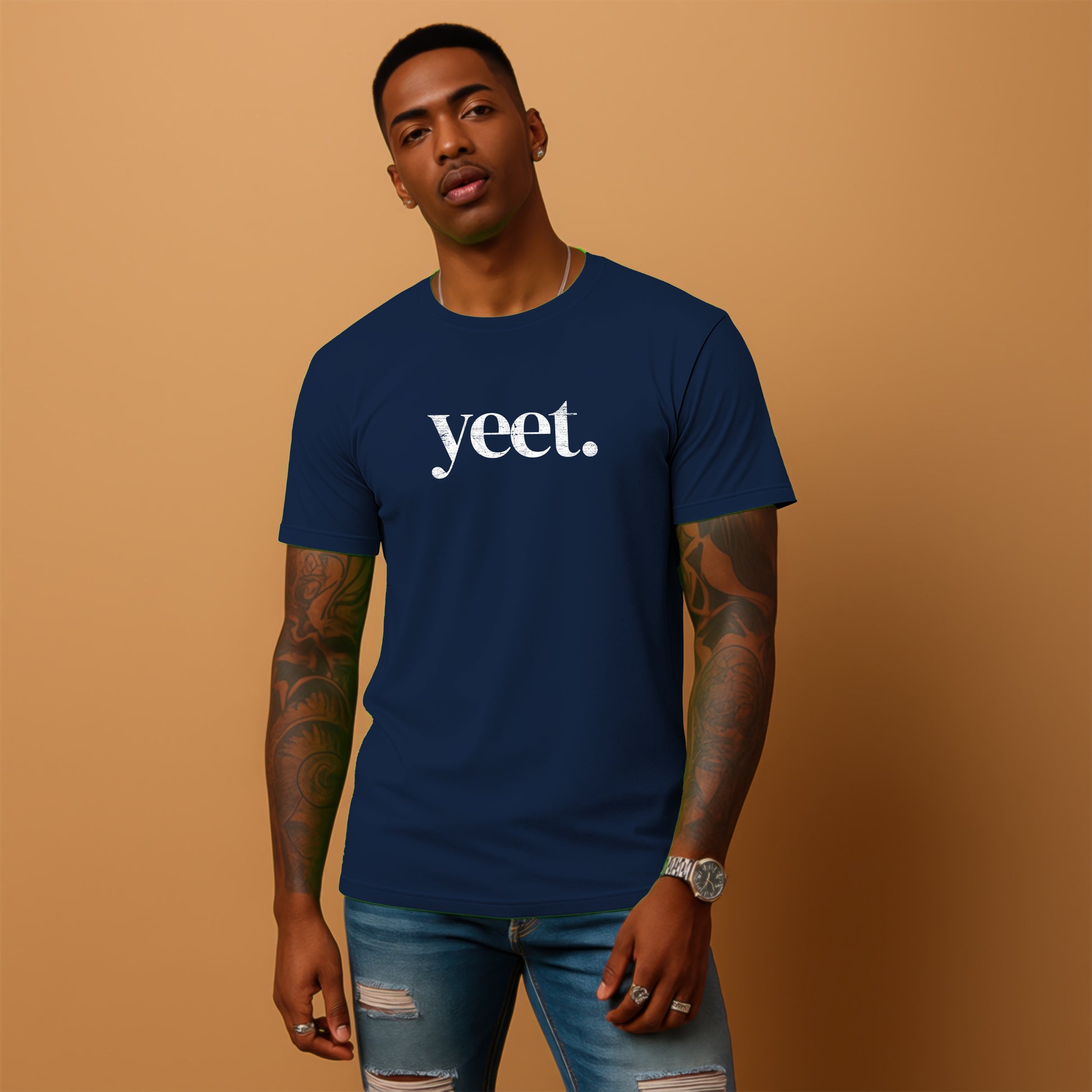 A man wearing a navy blue t-shirt with the word "yet" printed on it, standing against a peach-colored background.